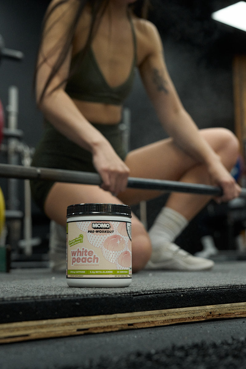 Woman preparing for a deadlift with MOMO White Peach Pre-Workout in the foreground
