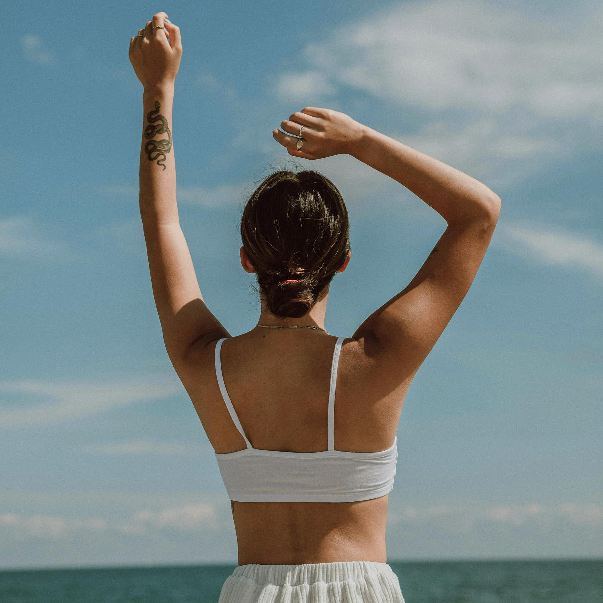 girl at the beach lifting her hands above her head taking in the sun