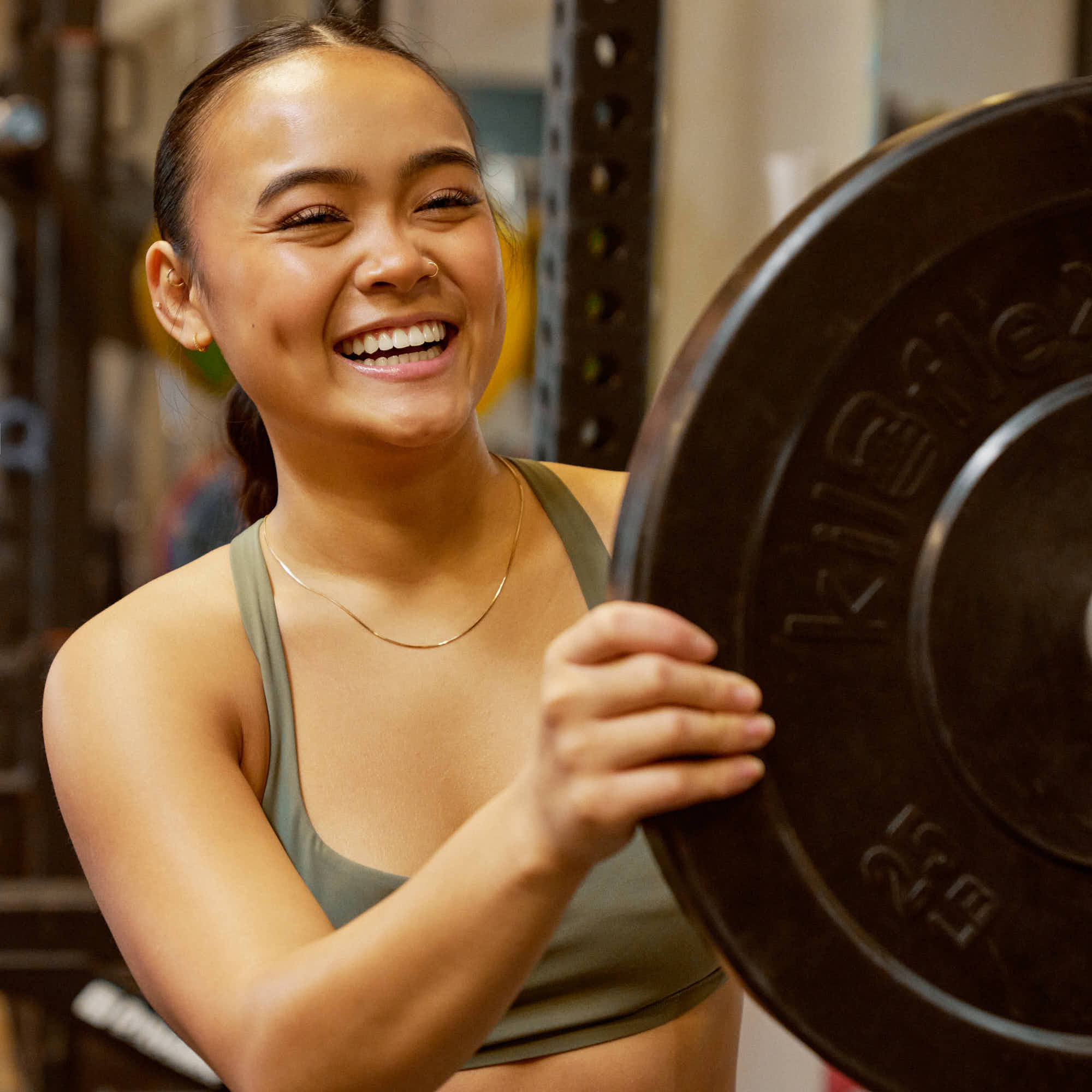 girl smiling as she puts a weight plate on the barbell on the squat rack