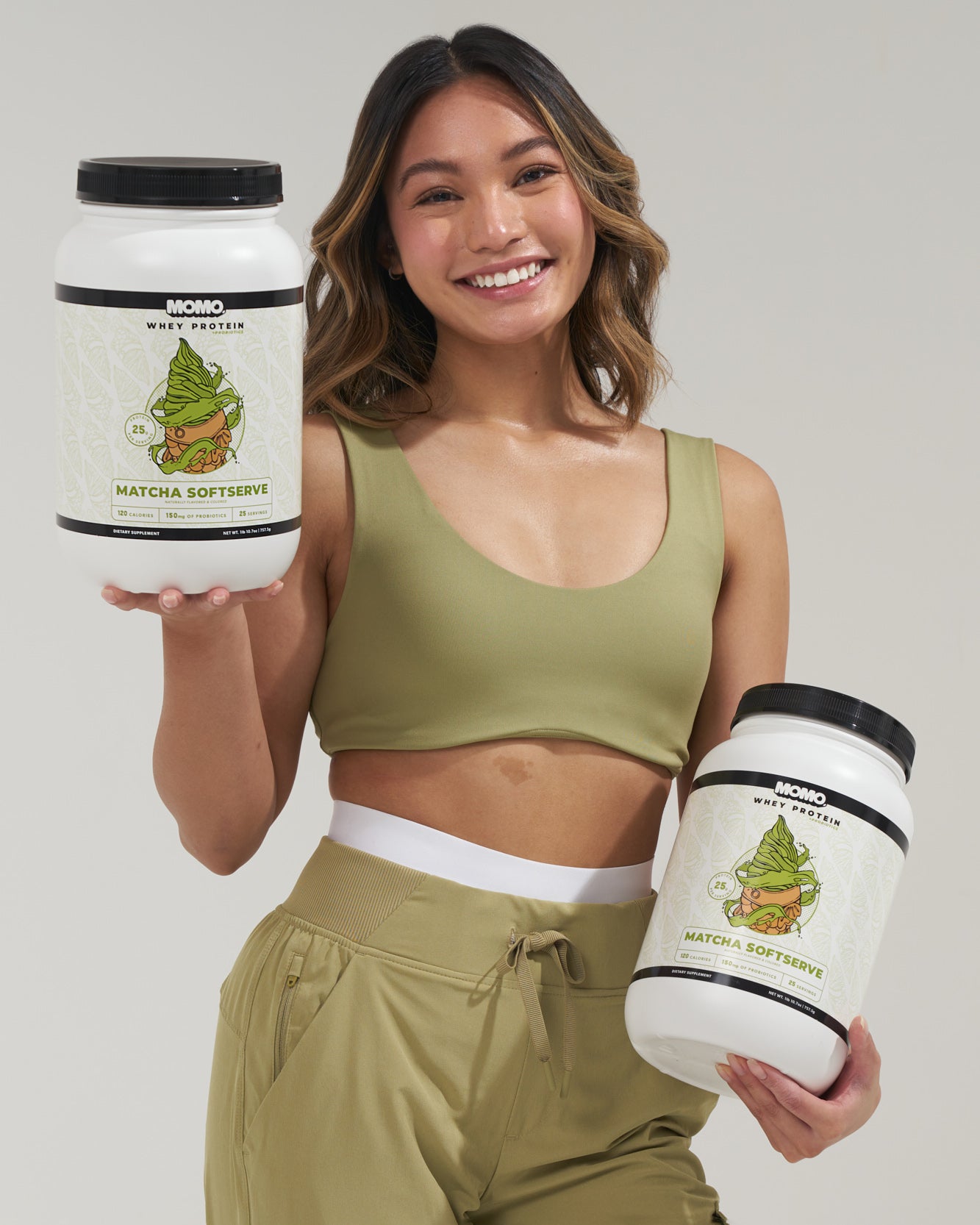 girl smiling while holding 2 MOMO Matcha soft serve flavored whey proteins