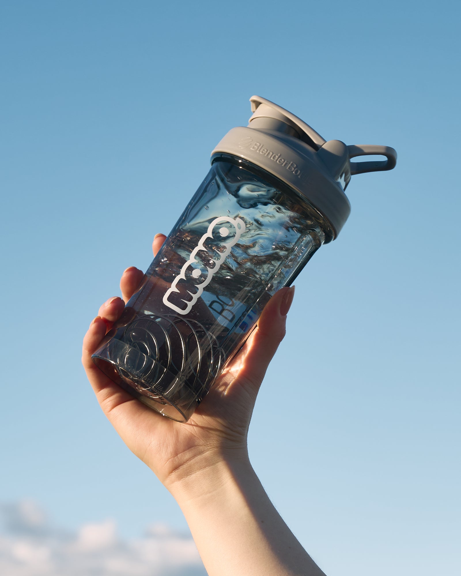 MOMO 24oz Smoke Gray BlenderBottle with wire whisk held towards the sky