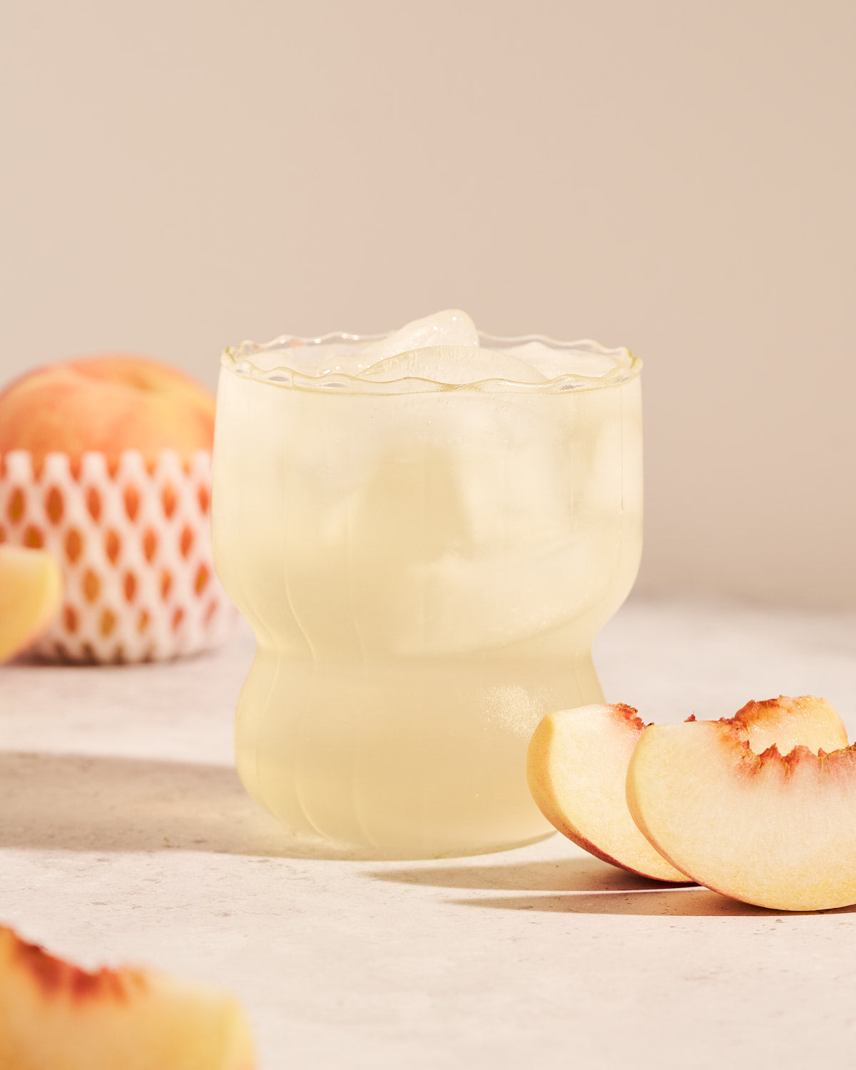 MOMO White Peach Pre-Workout in a clear glass with ice on a kitchen table, surrounded by peach slices.